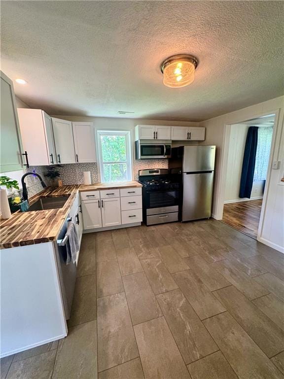 908 N 8th St, Lansing, KS 66043 - kitchen featuring appliances with stainless steel finishes, butcher block counters, white cabinets, a textured ceiling, and tasteful backsplash