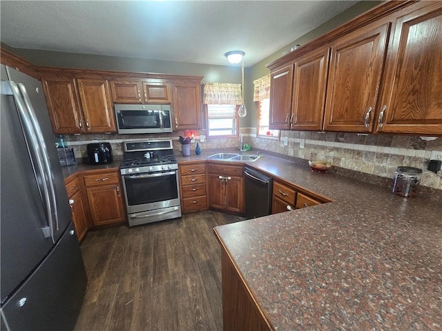657 SW Tisha Ln, Grain Valley, MO 64029 - kitchen with stainless steel appliances, a sink, dark countertops, and brown cabinetry