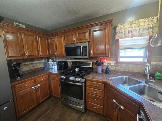 657 SW Tisha Ln, Grain Valley, MO 64029 - kitchen featuring appliances with stainless steel finishes, a sink, dark wood-style floors, brown cabinetry, and a textured ceiling