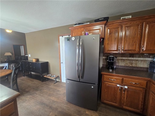657 SW Tisha Ln, Grain Valley, MO 64029 - kitchen with freestanding refrigerator, dark countertops, dark wood finished floors, brown cabinetry, and decorative backsplash