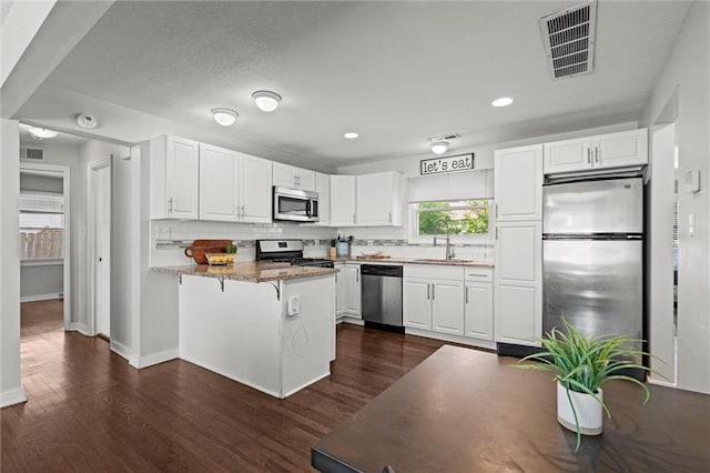 1304 6th Ave, Leavenworth, KS 66048 - kitchen with appliances with stainless steel finishes, a peninsula, dark wood-style floors, white cabinetry, and decorative backsplash