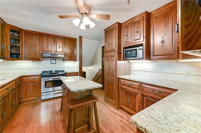 1131 Wildwood St, Leavenworth, KS 66048 - kitchen with stainless steel appliances, light wood finished floors, brown cabinetry, tasteful backsplash, and a textured ceiling