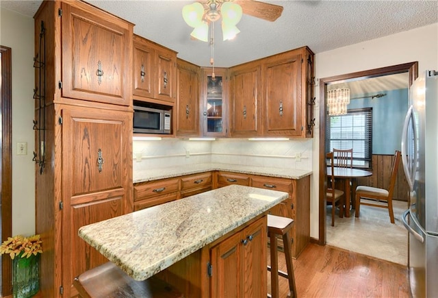 1131 Wildwood St, Leavenworth, KS 66048 - kitchen featuring stainless steel appliances, a kitchen breakfast bar, brown cabinets, light wood-style floors, and a textured ceiling