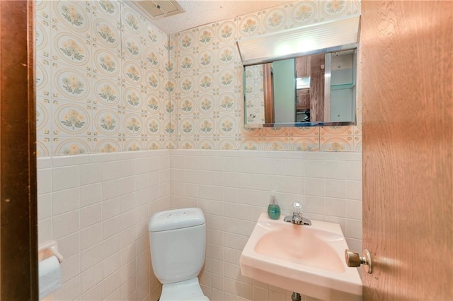 1131 Wildwood St, Leavenworth, KS 66048 - half bathroom with toilet, wallpapered walls, a sink, wainscoting, and tile walls