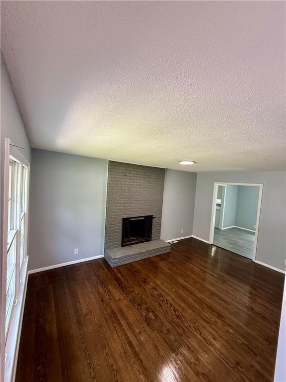 9203 James A Reed Rd, Kansas City, MO 64138 - unfurnished living room featuring a textured ceiling, a brick fireplace, wood finished floors, and baseboards
