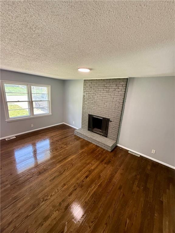 9203 James A Reed Rd, Kansas City, MO 64138 - unfurnished living room with a textured ceiling, wood finished floors, a fireplace, and baseboards