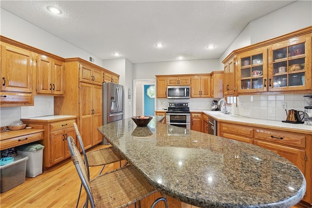 11580 S Skyview Ln, Olathe, KS 66061 - kitchen with appliances with stainless steel finishes, light wood finished floors, a kitchen breakfast bar, tasteful backsplash, and a textured ceiling