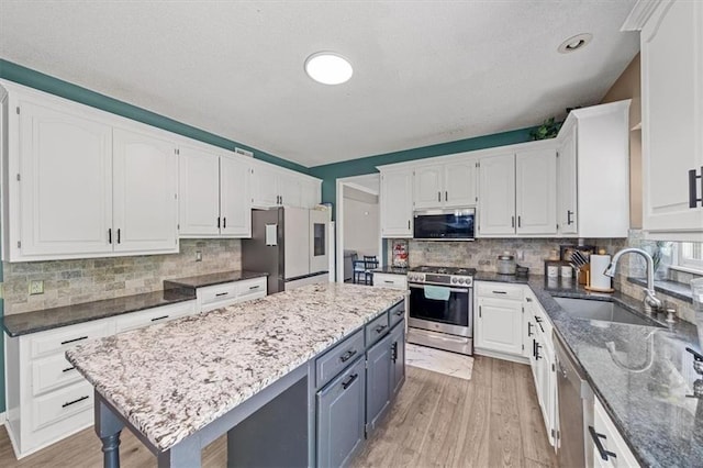 12890 S Greenwood St, Olathe, KS 66062 - kitchen featuring appliances with stainless steel finishes, a sink, white cabinetry, a kitchen island, and light wood-style flooring