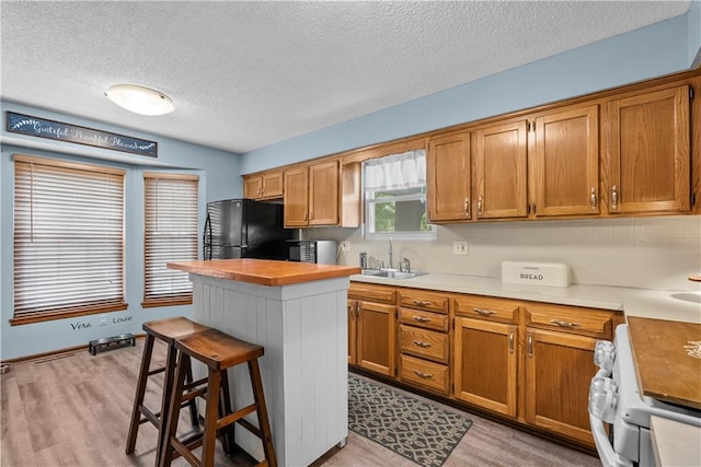 1805 N Lazy Branch Rd, Independence, MO 64058 - kitchen featuring a sink, freestanding refrigerator, a textured ceiling, a kitchen breakfast bar, and brown cabinetry