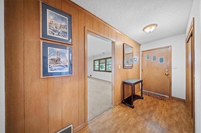 1107 E 110th St, Kansas City, MO 64131 - doorway featuring light wood-style floors, wooden walls, a textured ceiling, and baseboards