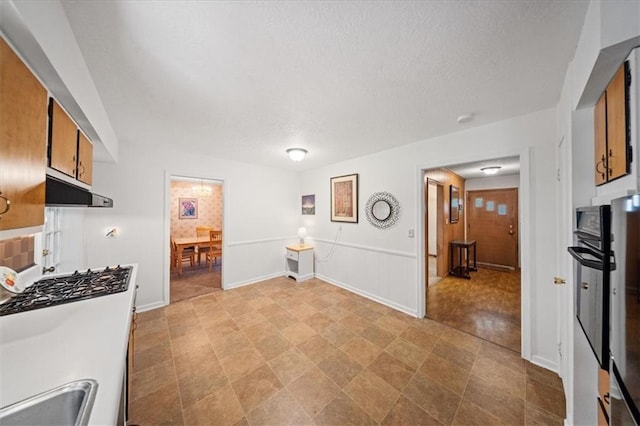 1107 E 110th St, Kansas City, MO 64131 - kitchen with range hood, wall oven, brown cabinets, a textured ceiling, and a sink