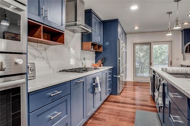 12204 Catalina St, Leawood, KS 66209 - kitchen featuring blue cabinets, wall chimney exhaust hood, appliances with stainless steel finishes, open shelves, and tasteful backsplash