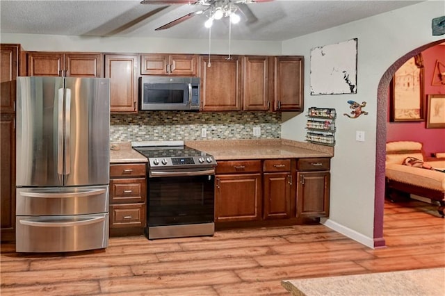 19490 Countryside Cir, Weston, MO 64098 - kitchen featuring appliances with stainless steel finishes, arched walkways, a ceiling fan, light wood finished floors, and a textured ceiling