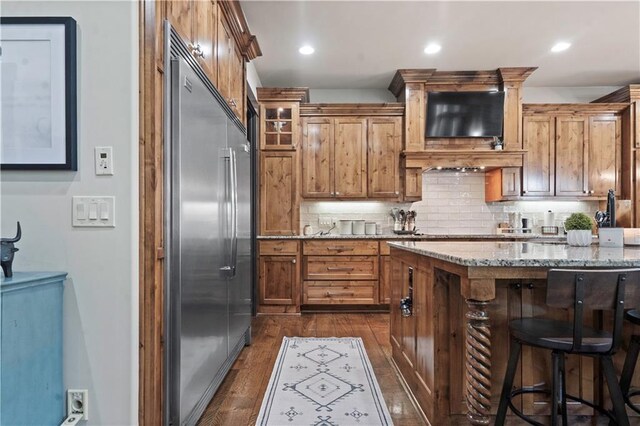 11106 W 146th Ter, Overland Park, KS 66221 - kitchen with built in refrigerator, light stone counters, dark wood-style flooring, backsplash, and a breakfast bar area