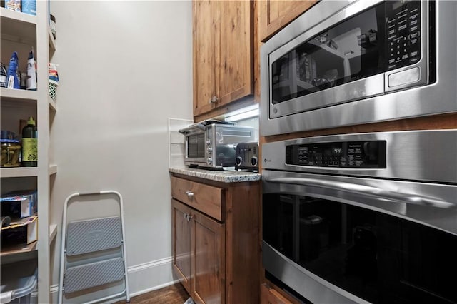 11106 W 146th Ter, Overland Park, KS 66221 - kitchen with stainless steel appliances, brown cabinetry, baseboards, and dark wood-type flooring