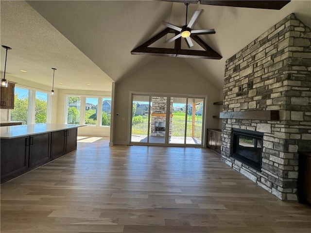 22415 87th Ter, Lenexa, KS 66227 - unfurnished living room featuring ceiling fan, high vaulted ceiling, a stone fireplace, wood finished floors, and beam ceiling