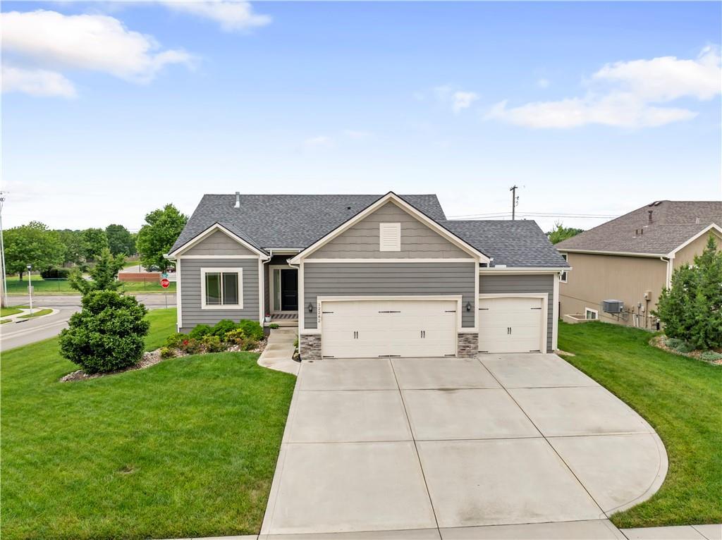 12282 S Pine St, Olathe, KS 66061 - view of front of home featuring driveway, a front yard, a garage, and stone siding