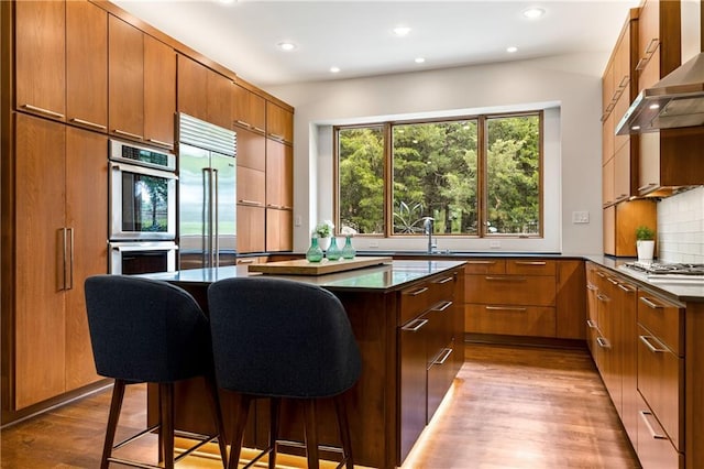 25075 W 105th Ter, Olathe, KS 66061 - kitchen with appliances with stainless steel finishes, wall chimney range hood, dark countertops, a kitchen island, and recessed lighting