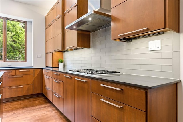25075 W 105th Ter, Olathe, KS 66061 - kitchen featuring wall chimney range hood, light wood-style flooring, decorative backsplash, and stainless steel gas stovetop