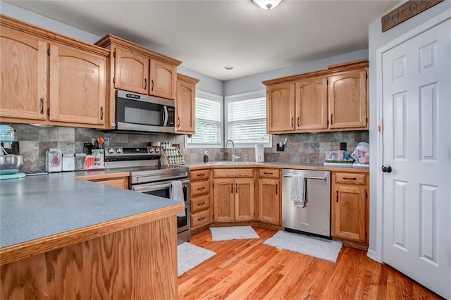 706 S Sunset Ln, Raymore, MO 64083 - kitchen with appliances with stainless steel finishes, a sink, light wood-style flooring, tasteful backsplash, and light countertops