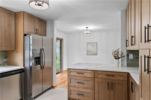 4417 E 104th St, Kansas City, MO 64137 - kitchen with stainless steel appliances, a chandelier, backsplash, brown cabinetry, and a peninsula