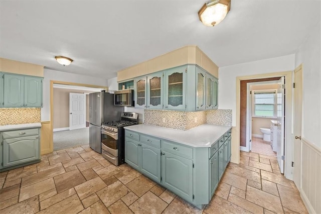 2306 Red Bridge Ter, Kansas City, MO 64131 - kitchen featuring appliances with stainless steel finishes, stone tile floors, light countertops, decorative backsplash, and glass insert cabinets
