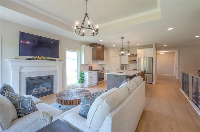 24129 W 95th St, Lenexa, KS 66227 - living area with a tiled fireplace, a tray ceiling, recessed lighting, a chandelier, and light wood-type flooring