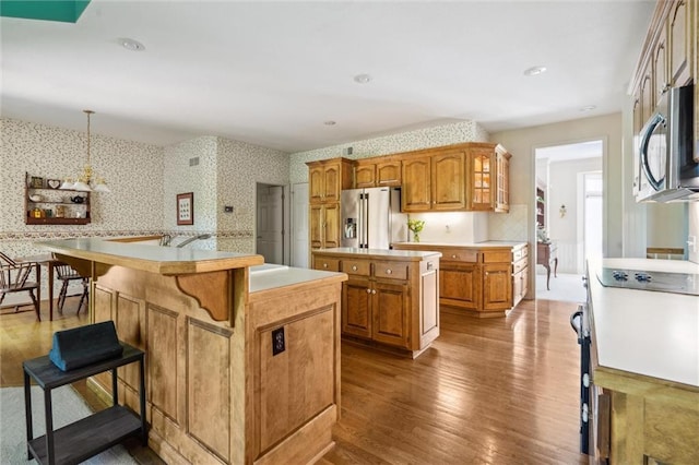 14913 W 72nd St, Shawnee, KS 66216 - kitchen with wallpapered walls, stainless steel appliances, a kitchen island, wood finished floors, and light countertops
