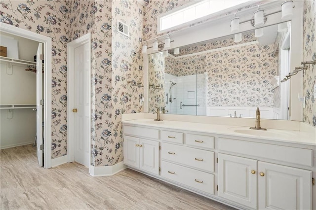 14913 W 72nd St, Shawnee, KS 66216 - full bathroom with wallpapered walls, a shower stall, double vanity, a spacious closet, and wood finished floors