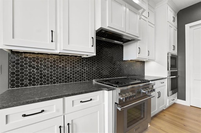 9412 Aurora St, Lenexa, KS 66220 - kitchen with appliances with stainless steel finishes, dark countertops, white cabinets, light wood-style flooring, and decorative backsplash