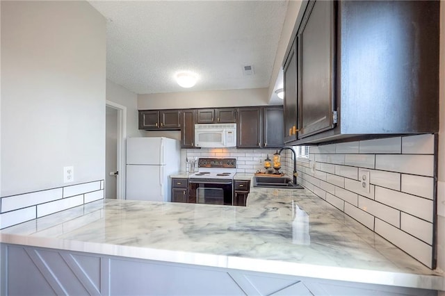 2406 Alabama St Unit 9D, Lawrence, KS 66046 - kitchen with white appliances, tasteful backsplash, a peninsula, dark brown cabinetry, and light stone countertops