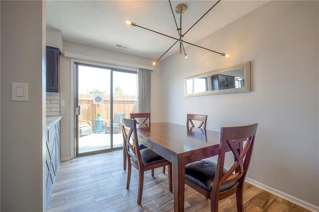 2406 Alabama St Unit 9D, Lawrence, KS 66046 - dining area featuring light wood finished floors, a textured ceiling, and a chandelier
