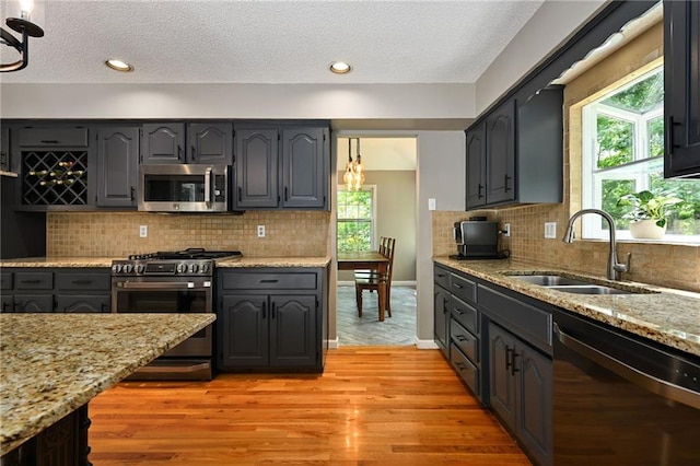 8 Apache Dr, Lake Winnebago, MO 64034 - kitchen featuring appliances with stainless steel finishes, a sink, light wood finished floors, light stone counters, and a textured ceiling