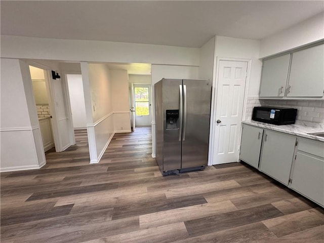 7703 E 107th St, Kansas City, MO 64134 - kitchen with stainless steel fridge, black microwave, dark wood finished floors, light countertops, and decorative backsplash