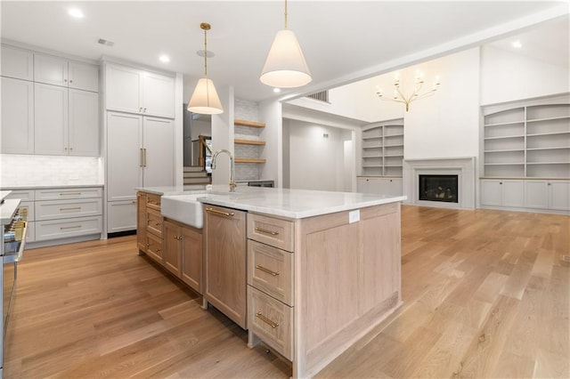 18568 W 180th Ct, Olathe, KS 66062 - kitchen featuring a sink, light wood-style flooring, an island with sink, a fireplace, and pendant lighting