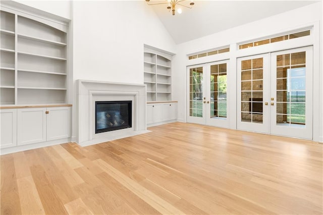 18568 W 180th Ct, Olathe, KS 66062 - unfurnished living room featuring french doors, light wood-style flooring, a fireplace with flush hearth, built in features, and high vaulted ceiling