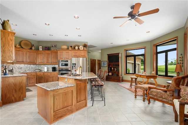 1672 N 1st Rd, Baldwin City, KS 66006 - kitchen with appliances with stainless steel finishes, a center island with sink, a kitchen bar, backsplash, and light stone countertops