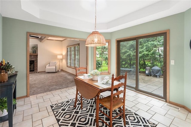 2101 Riviera Dr, Lawrence, KS 66047 - dining area featuring a raised ceiling, light carpet, a brick fireplace, and baseboards