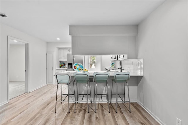 44 G St, Lake Lotawana, MO 64086 - kitchen with a peninsula, light wood finished floors, white cabinetry, a breakfast bar, and light countertops