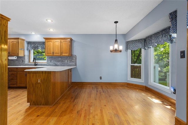 2432 SE 6th St, Lees Summit, MO 64063 - kitchen featuring brown cabinetry, decorative backsplash, a chandelier, and light wood-style floors