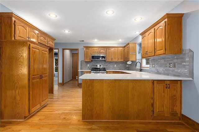 2432 SE 6th St, Lees Summit, MO 64063 - kitchen featuring stainless steel appliances, a peninsula, brown cabinets, light countertops, and light wood-style floors