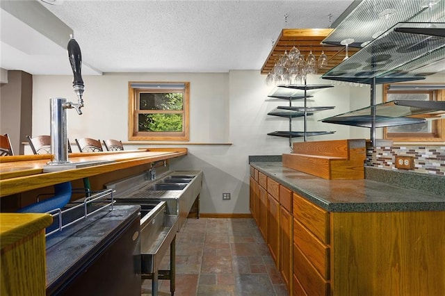 2432 SE 6th St, Lees Summit, MO 64063 - kitchen with brown cabinets, dark countertops, dark stone finish flooring, tasteful backsplash, and a textured ceiling