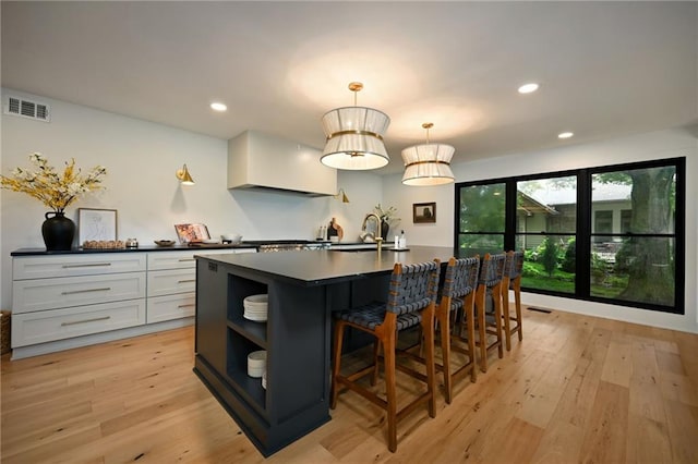 110 Cherokee Ln, Lake Winnebago, MO 64034 - kitchen with dark countertops, open shelves, light wood-style flooring, a kitchen island with sink, and a breakfast bar area