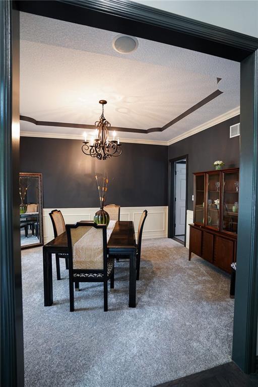3832 SW Boulder Dr, Lees Summit, MO 64082 - carpeted dining room featuring crown molding, a chandelier, a wainscoted wall, a textured ceiling, and a decorative wall