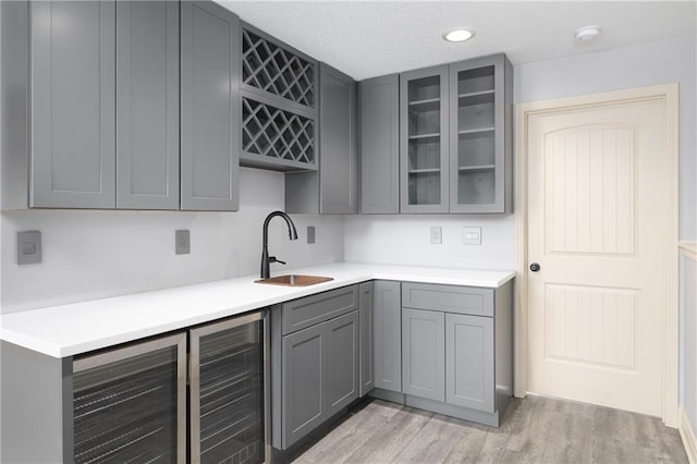 486 S 137th Pl, Bonner Springs, KS 66012 - kitchen with gray cabinets, a sink, light wood-style flooring, glass insert cabinets, and wine cooler