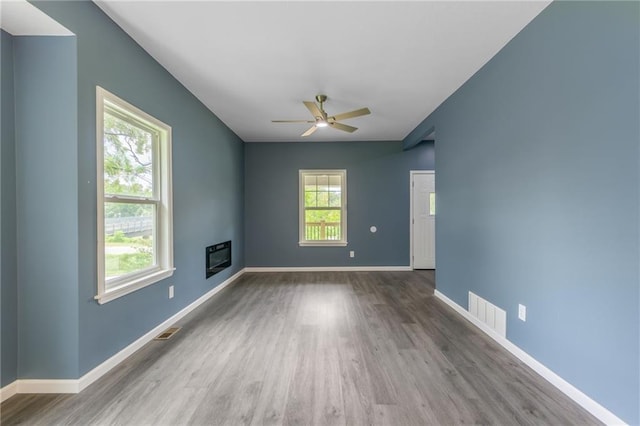 4233 Euclid Ave, Kansas City, MO 64130 - spare room featuring wood finished floors, a glass covered fireplace, a ceiling fan, and baseboards