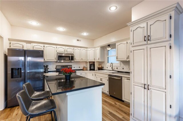 5916 NE Turquoise Dr, Lees Summit, MO 64064 - kitchen featuring appliances with stainless steel finishes, a sink, tasteful backsplash, a center island, and light wood-style flooring