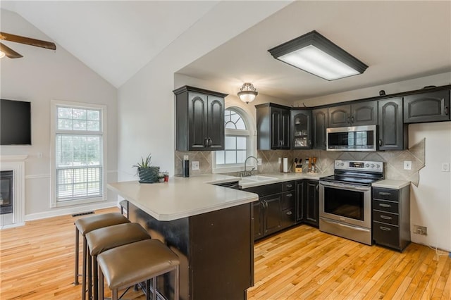 1955 Birmingham Rd, Liberty, MO 64068 - kitchen with appliances with stainless steel finishes, a peninsula, light wood-type flooring, a breakfast bar area, and vaulted ceiling