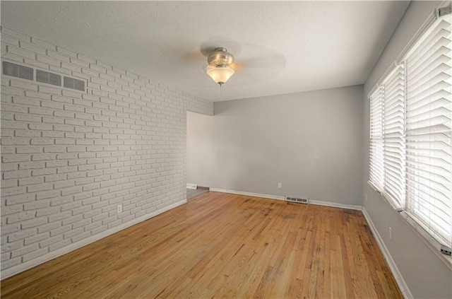 2917 N 83rd Ter, Kansas City, KS 66109 - spare room featuring brick wall, ceiling fan, light wood finished floors, baseboards, and a textured ceiling