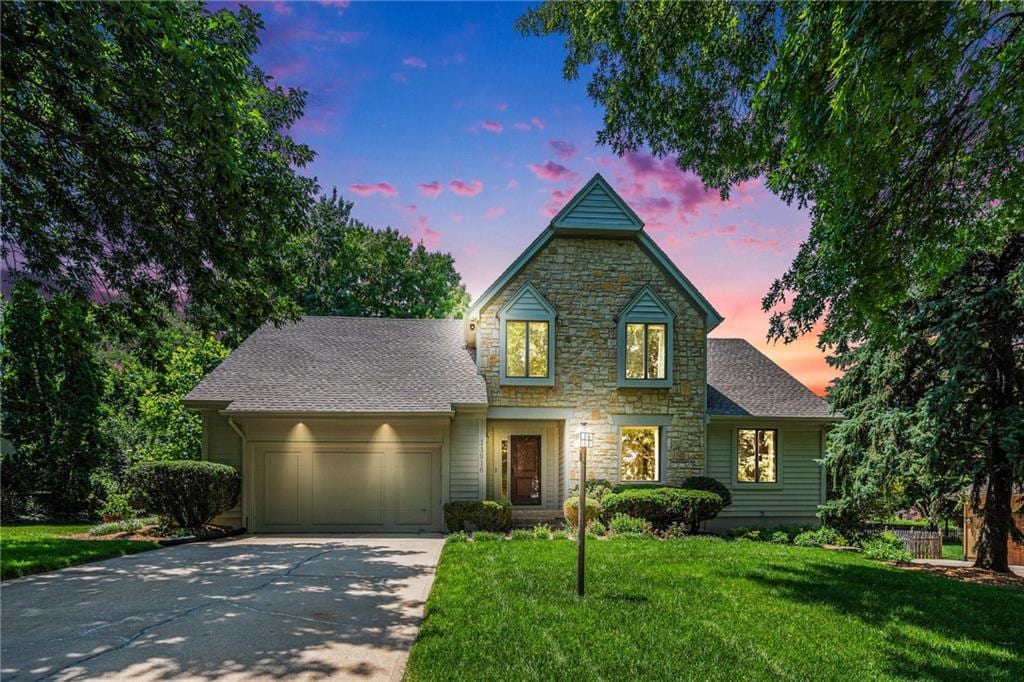 11916 Wenonga Ln, Leawood, KS 66209 - traditional home featuring stone siding, an attached garage, driveway, a yard, and roof with shingles